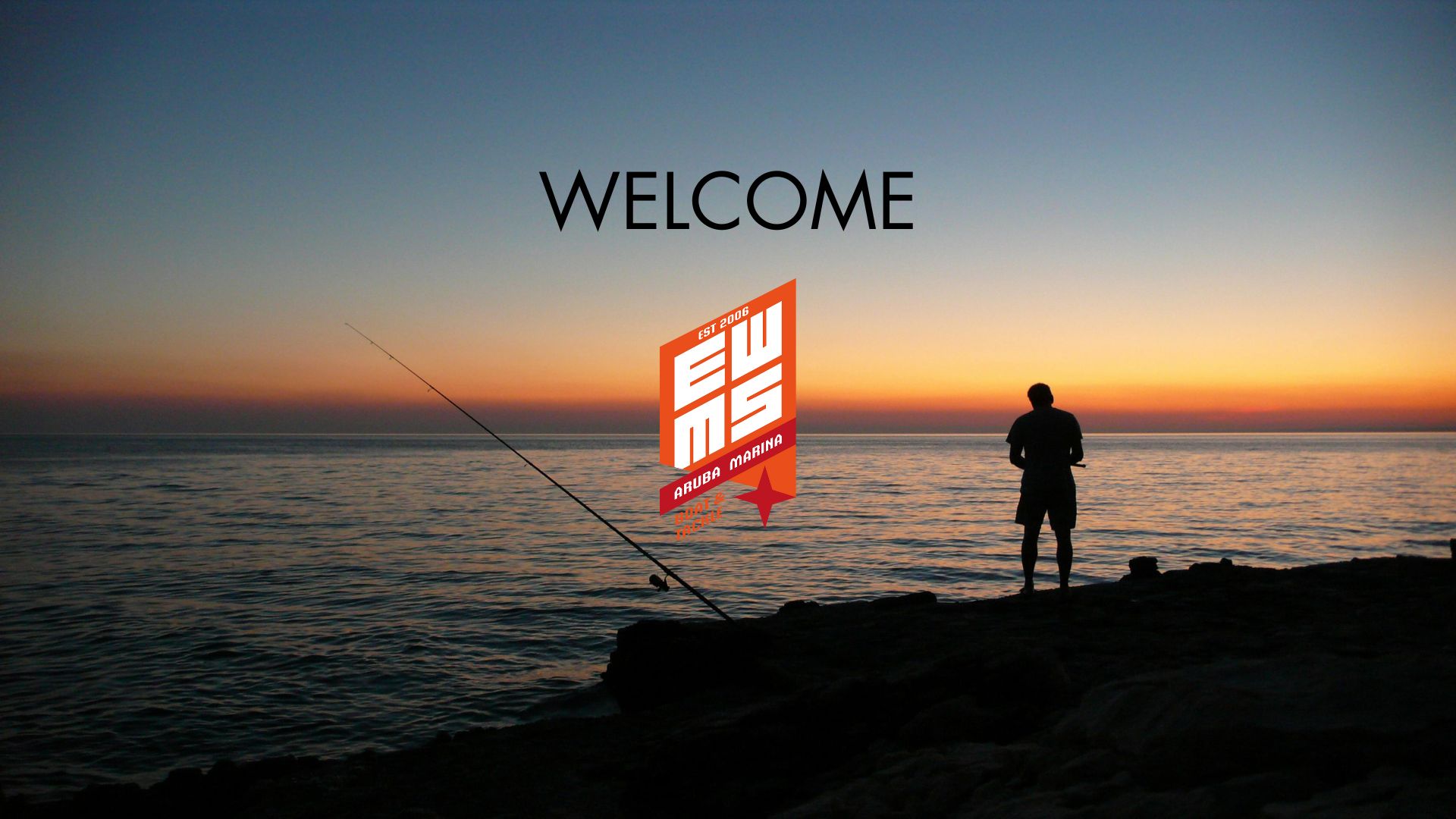 Silhouette of a person fishing at the edge of a calm sea during a vibrant sunset, with the sky transitioning from deep blue to warm orange hues.